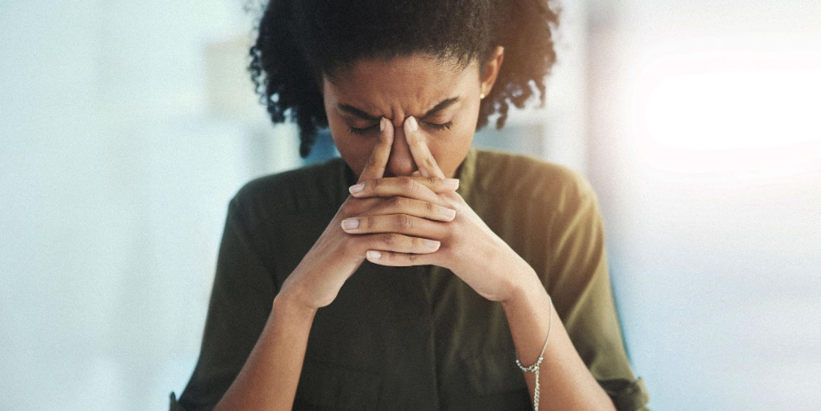 Woman wearing green is frowning and holding her hands to her face due to thyroid issues