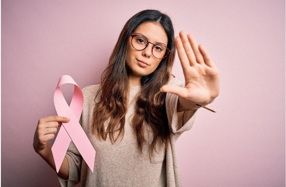 Une jeune femme brune tenant le ruban rose du cancer du sein dans une main et levant l'autre pour signaler l'arrêt du cancer du sein.