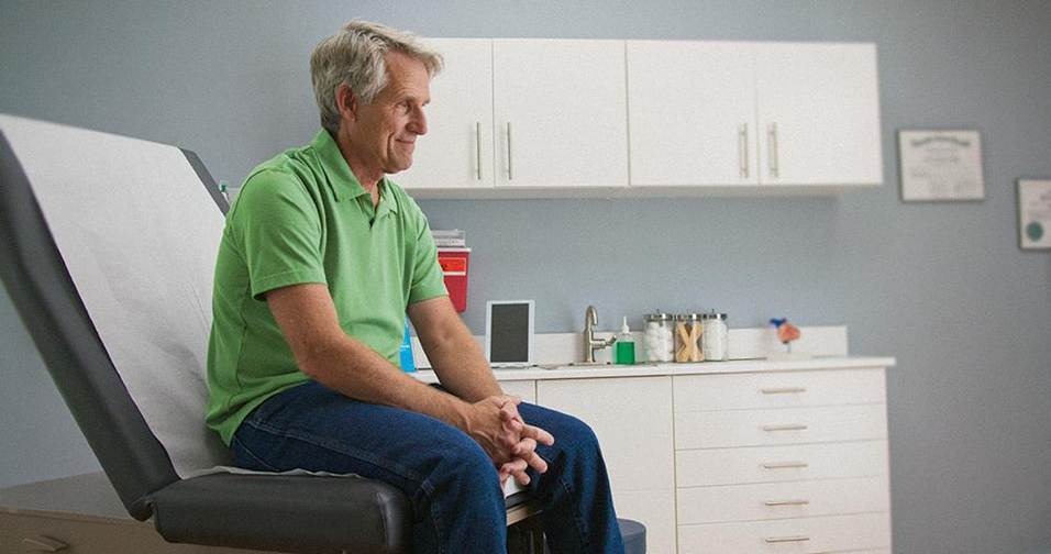 Patient caucasien âgé attendant le médecin lors d'un contrôle annuel, assis sur une table de salle d'examen.