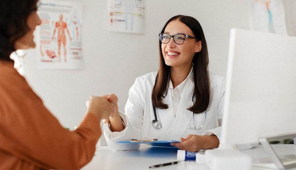 Une femme médecin et une patiente souriantes se serrent la main lors d'un examen médical dans le cabinet du médecin.