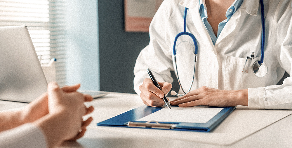 A female doctor writing a medical prescription or referral for a patient during a routine check-up.