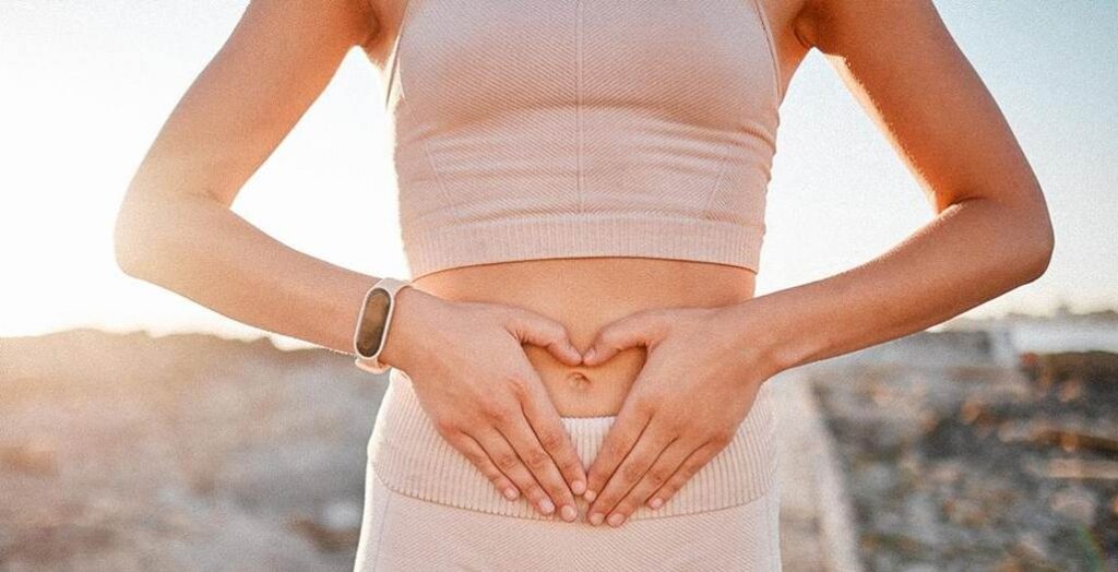 Gros plan d'une femme formant un cœur avec ses mains posées sur son utérus.