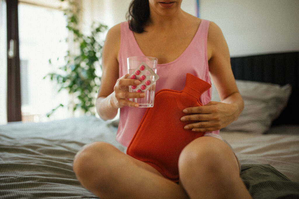 Jeune femme tenant un verre d'eau, des analgésiques et une bouillotte pour soulager des douleurs abdominales et ovariennes.
