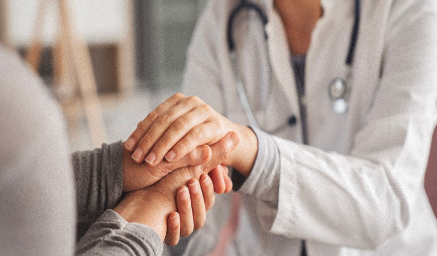 Close up of a doctor holding a patient's hands with compassion and care.