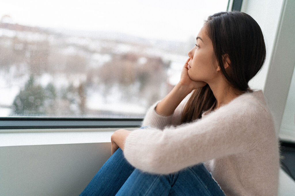 Woman sitting by a window and looking outside at a snowy winter scene.