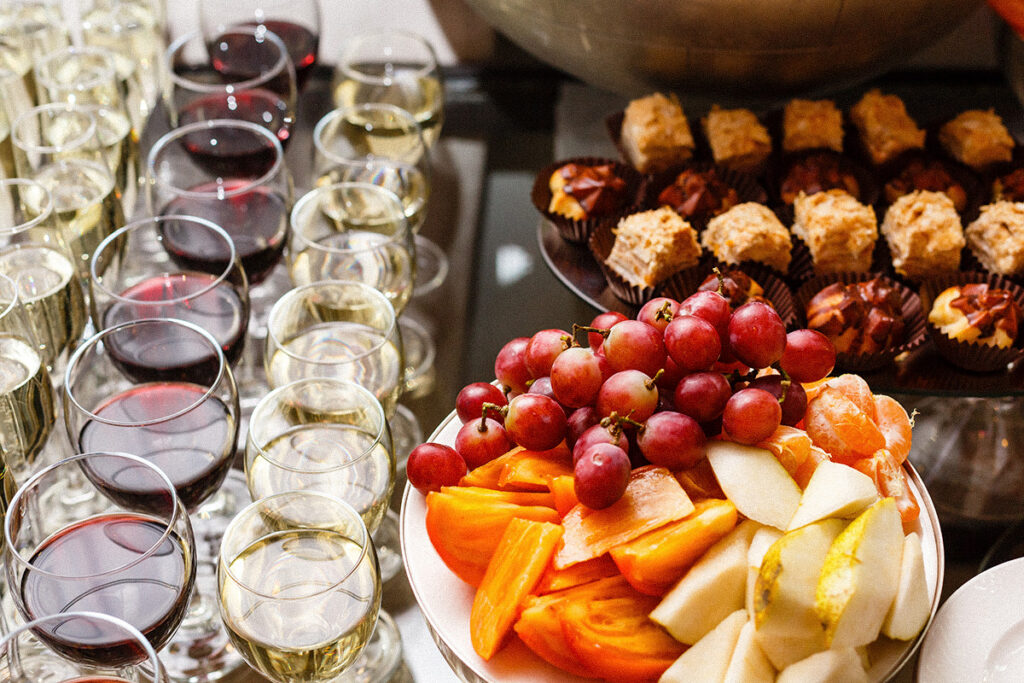 Glasses of red and white wine beside a holiday spread of fresh fruit and desserts.